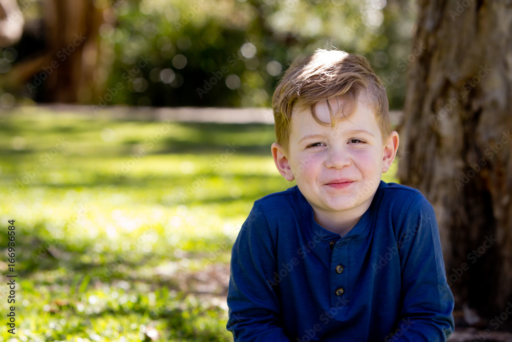 Young boy quietly sitting crossed legged against tree trunk in park - with copy space Young boy quietly sitting crossed legged against tree trunk in park - with copy space