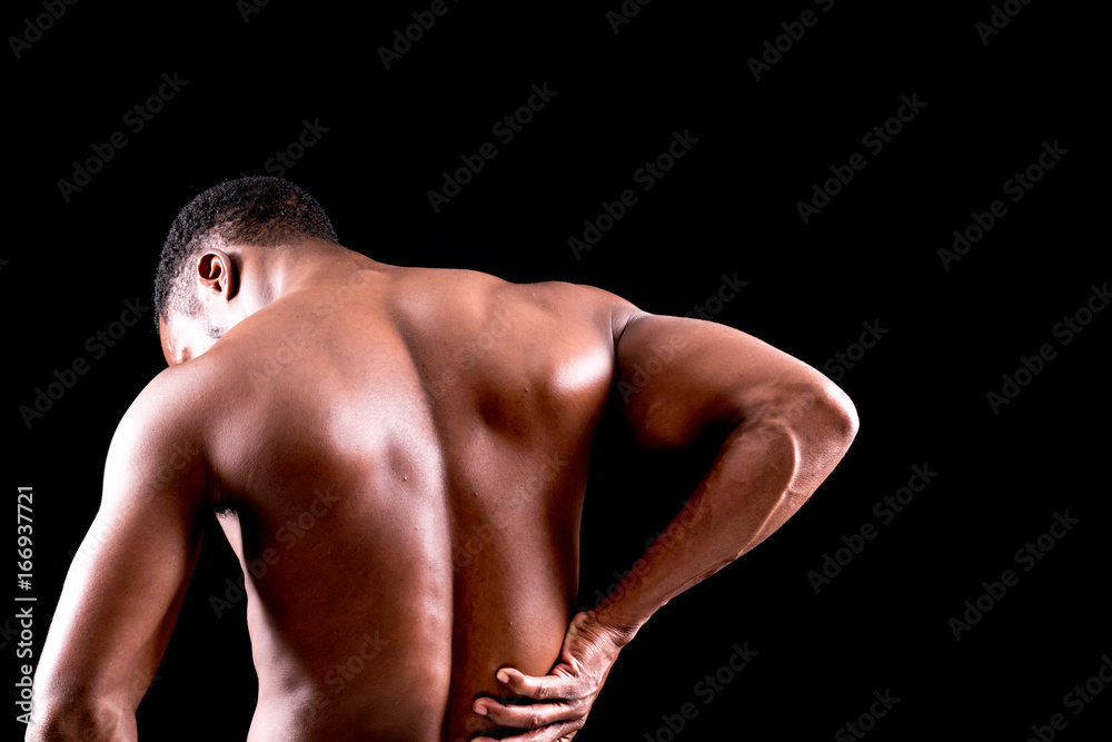 Rear view of a young man holding his back in pain on black