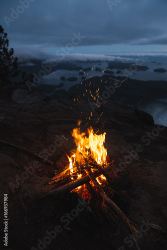 Rim with campfire above bay with islands and forests in cloudy weather from top view in the evening