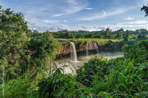 Dry Nur waterfall in Vietnam, the coast is covered with lush green tropical vegetation, against the backdrop of clouds and blue sky