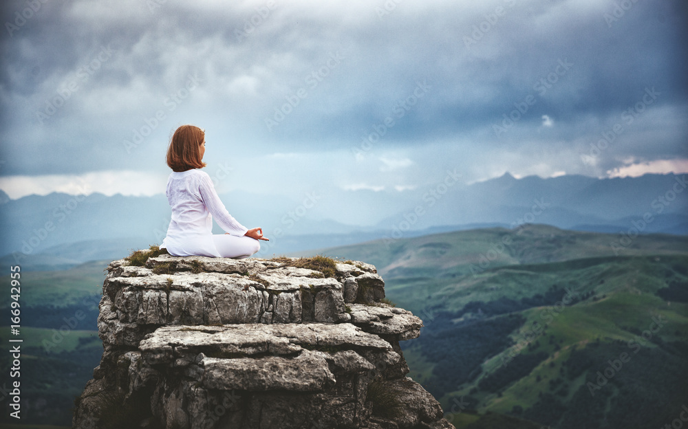 woman practices yoga and meditates in   lotus position on mountains, peak