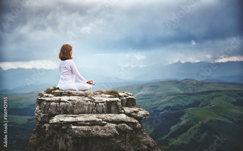 woman practices yoga and meditates in lotus position on mountains, peak