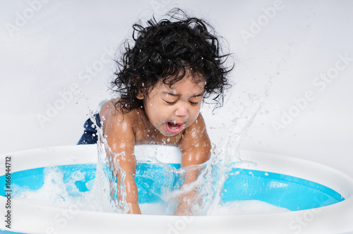 infant splashing water in bath tub, timely splash, hispanic boy