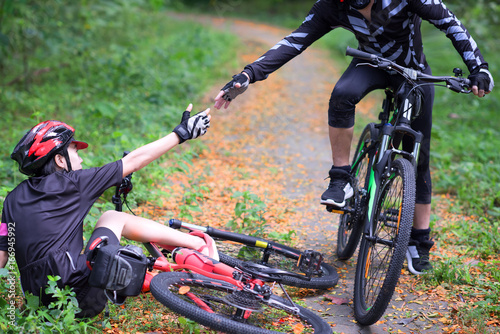 hand of cyclist woman try to reach hand of cyclist man to help supports after an accident in the jungle forest