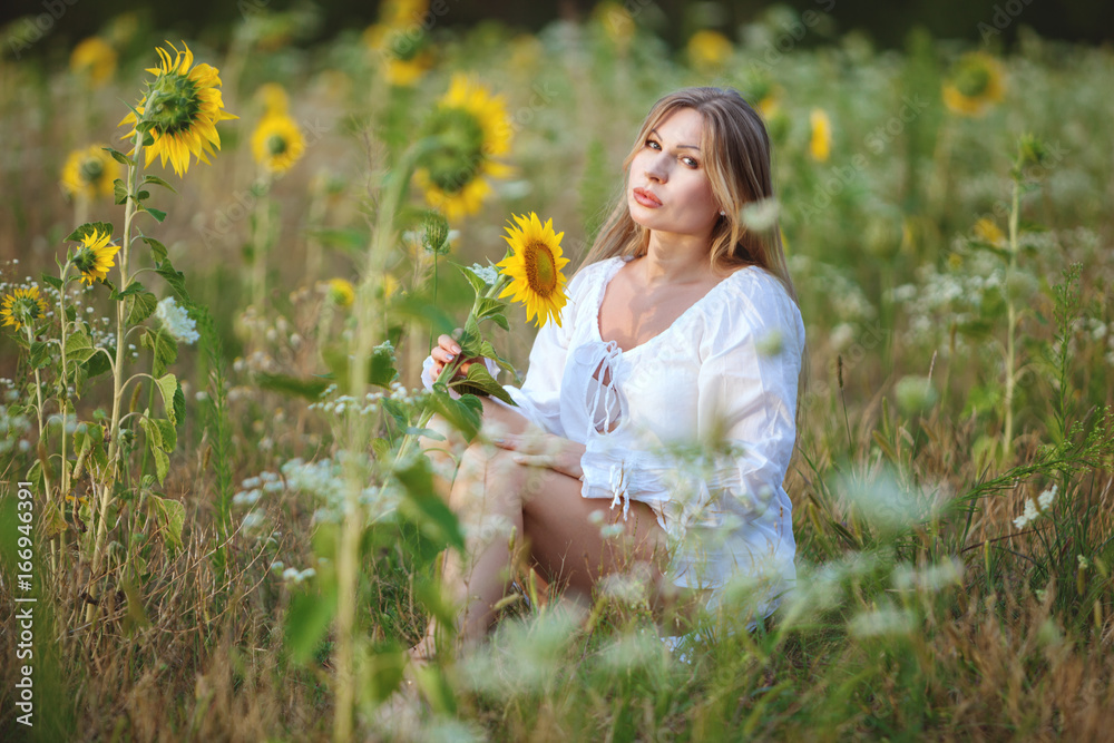 Young woman sitting in a field among sunflowers, on a bright summer day. Young woman sitting in a field among sunflowers, on a bright summer day.