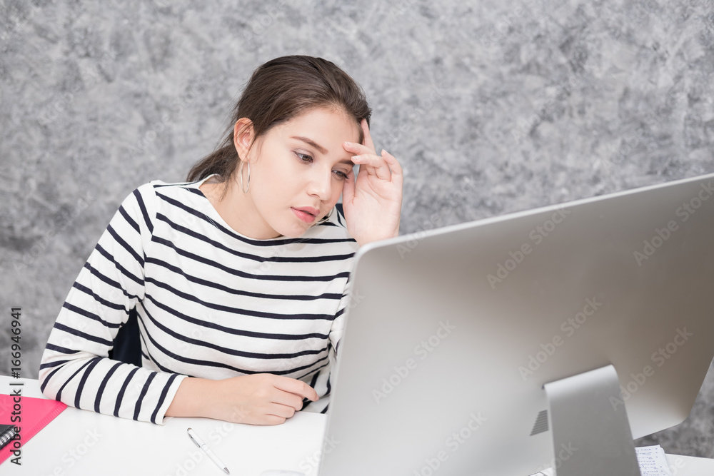 Beautiful young woman looking at a computer screen and thinking at the office, stressed and nervous Beautiful young woman looking at a computer screen and thinking at the office, stressed and nervous