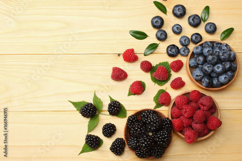 фотографія mix of blueberries, blackberries, raspberries in wooden bowl on light wooden table background