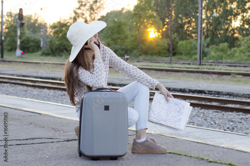 Yong long hair girl with lugguage and map on hand talking on mobile phone at train station photo