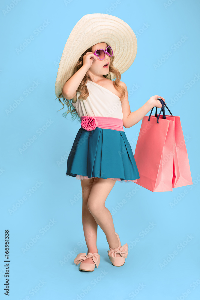 The cute little caucasian brunette girl in dress holding shopping bags The cute little caucasian brunette girl in dress holding shopping bags