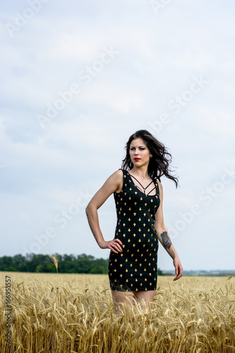 Vintage style, relaxing young woman in nature on a golden field. Rest in a meadow in the summer sun. Portrait beautiful girl, wind fluttering hair, lady in black dress with gold crosses 