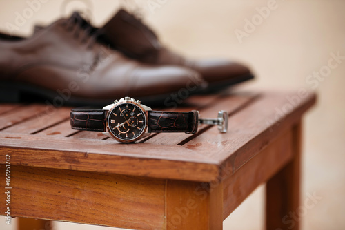 Expensive man wrist metal watch with leather strap and shoes on background