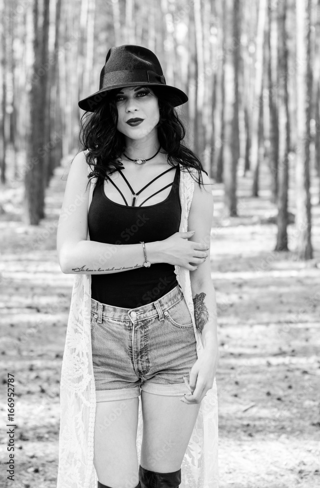 Enigmatic curly brunette woman with gothic make up and black fedora hat,  white lace cardigan, in