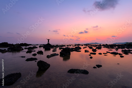 Silhouette of young man raised hands on rock, tropical beach at sunset © yotrakbutda