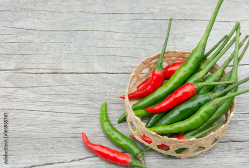 Fresh chili peppers, red and green are in the little basket woven from bamboo. Placed on the wooden floor.