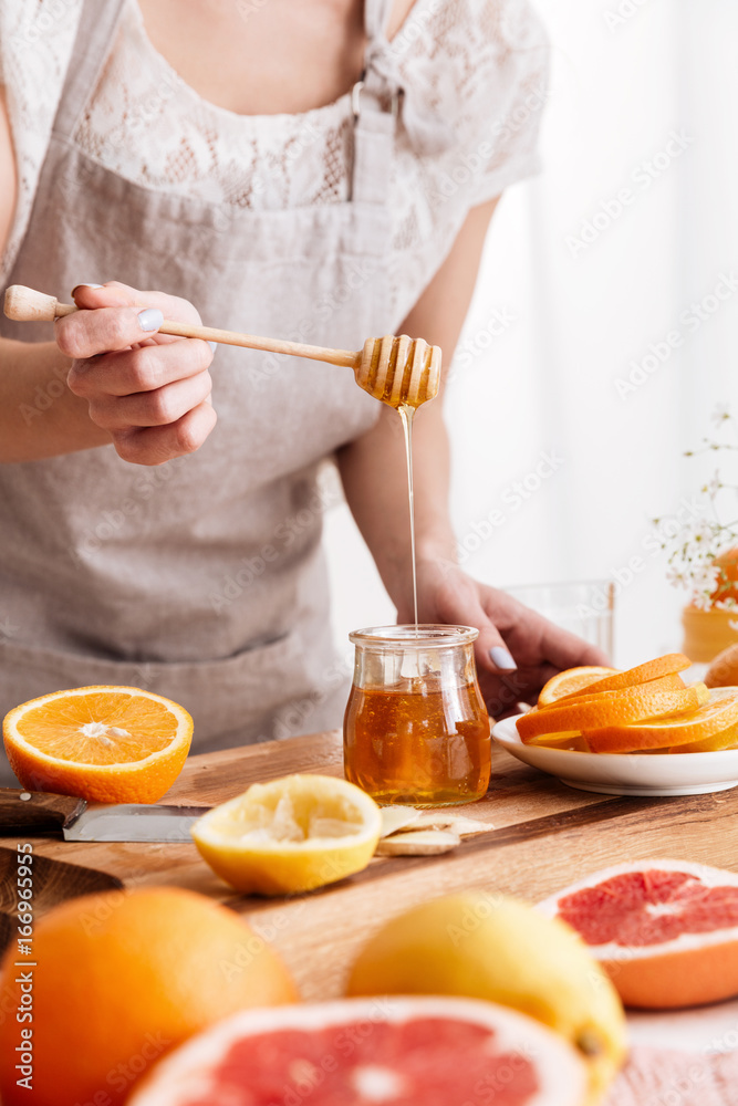 Woman standing near table with citruses and holding honey. Woman standing near table with citruses and holding honey.