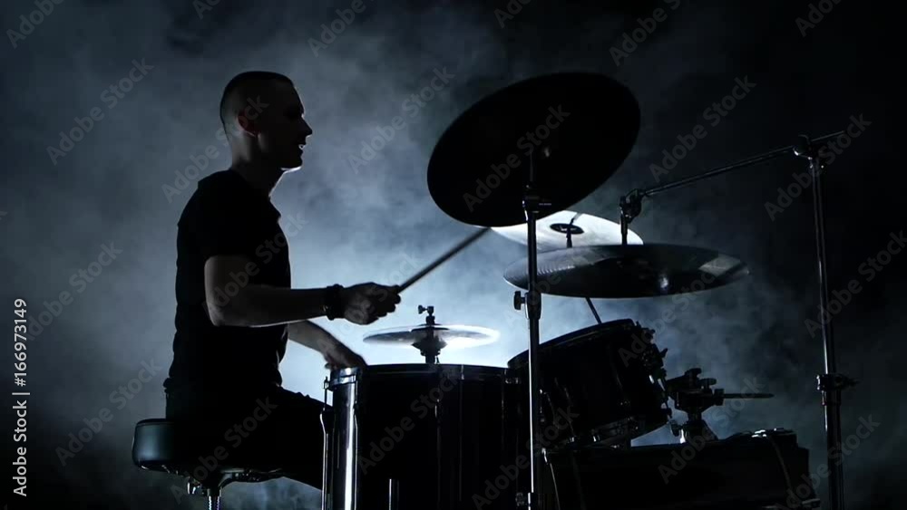 Energetic musician plays good music on drums. Black smoky background . Side view. Silhouette. Slow motion