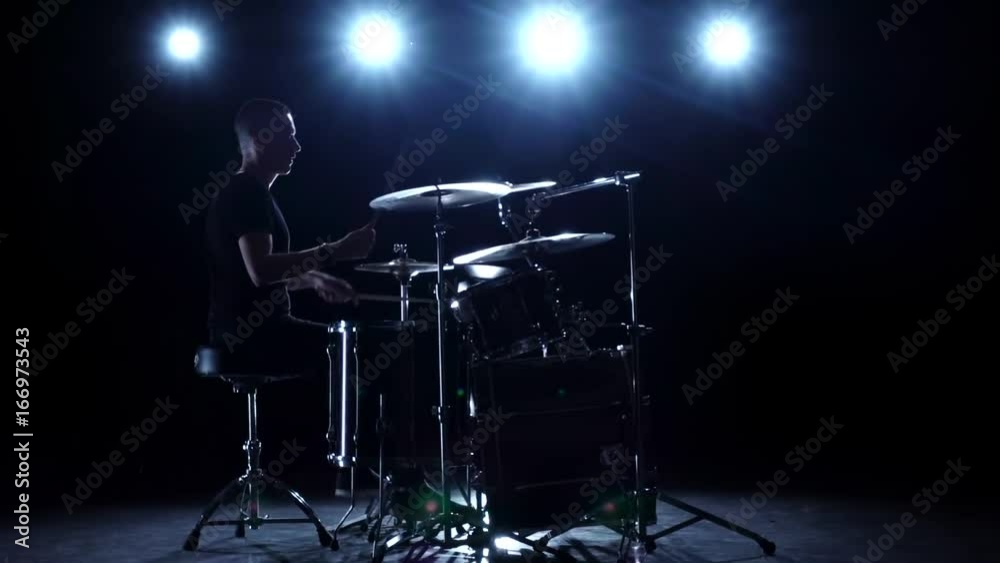 Drummer plays the melody on the drums energetically. Black background. Back light. Silhouette. Slow motion