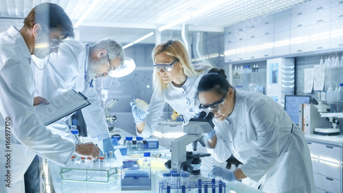 Team of Medical Research Scientists Work on a New Generation Disease Cure. They use Microscope, Test Tubes, Micropipette and Writing Down Analysis Results. Laboratory Looks Busy, Bright and Modern. photo