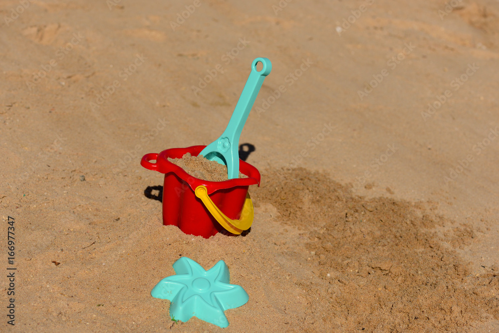 Baby beach toys - bucket, shovel and pask in the sand on a sunny day Baby beach toys - bucket, shovel and pask in the sand on a sunny day