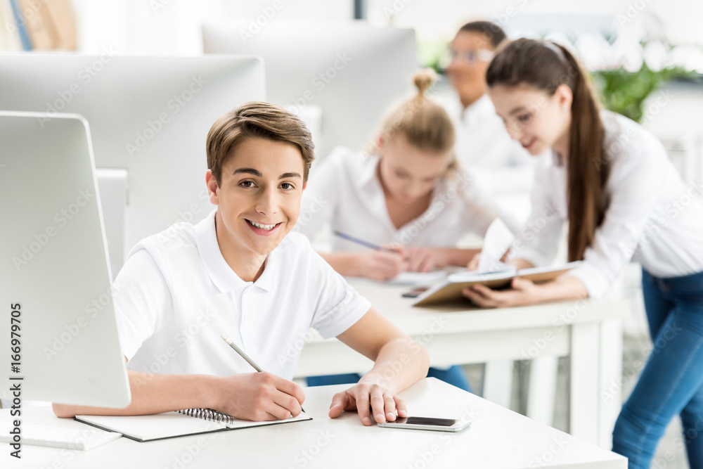 portrait of smiling student looking at camera while sitting at table during lesson in classroom portrait of smiling student looking at camera while sitting at table during lesson in classroom