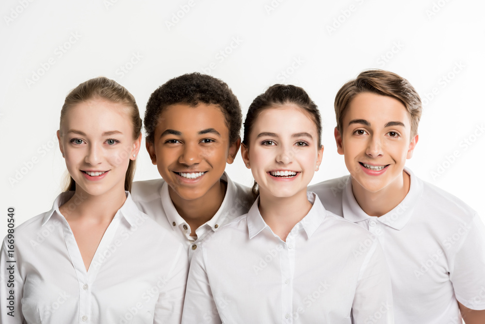 portrait of smiling multiethnic teenagers in white shirts looking at camera isolated on white