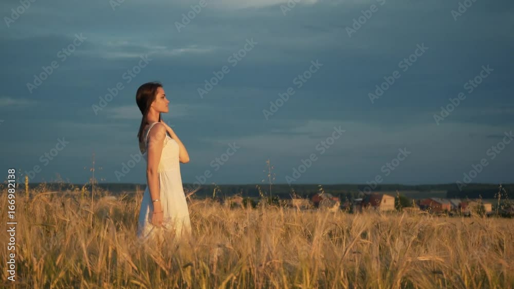 a young girl stands in a Golden field of wheat at sunset and raises his hands up, slow motion a young girl stands in a Golden field of wheat at sunset and raises his hands up, slow motion