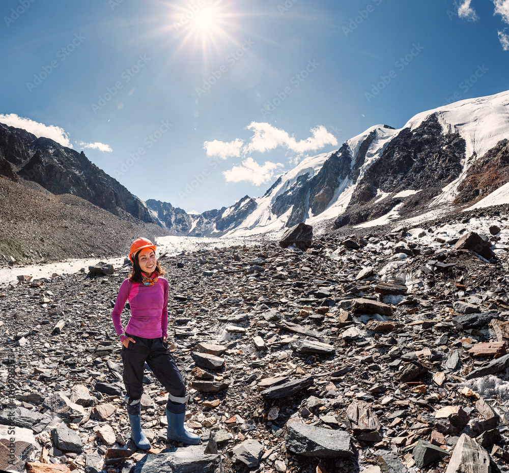 Young female mountaineer in a helmet near the top of the mountain pass in the middle of rocks and glaciers