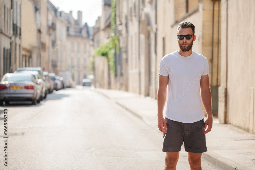 Obraz premium Hipster handsome male model with beard wearing white blank t-shirt with space for your logo or design in casual urban style
