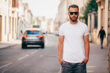 Hipster handsome male model with beard wearing white blank t-shirt with space for your logo or design in casual urban style