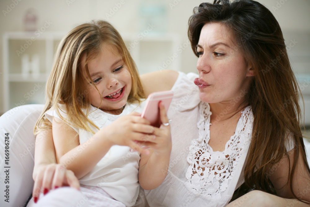 Smiling mother with daughter using smart phone on bed. Smiling mother with daughter using smart phone on bed.