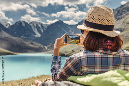 woman hiker taking photo of a mountain lake on her smartphone