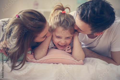 Family with one daughter lying on bed.