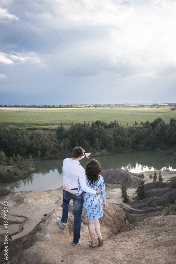 A loving couple looks at the blue lake against the background of clouds and learn the sun A loving couple looks at the blue lake against the background of clouds and learn the sun