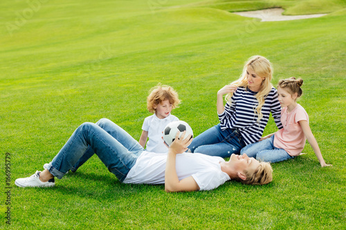 happy young family with soccer ball resting on green grass in park © LIGHTFIELD STUDIOS
