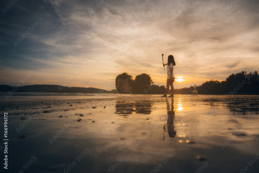 Beautiful young woman doing selfie on the beach with sunset. woman selfie on the beach.