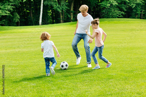 happy young father with two adorable children playing soccer on green lawn at park