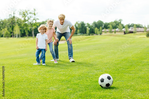 happy father with daughter and son looking at soccer ball while standing on grass