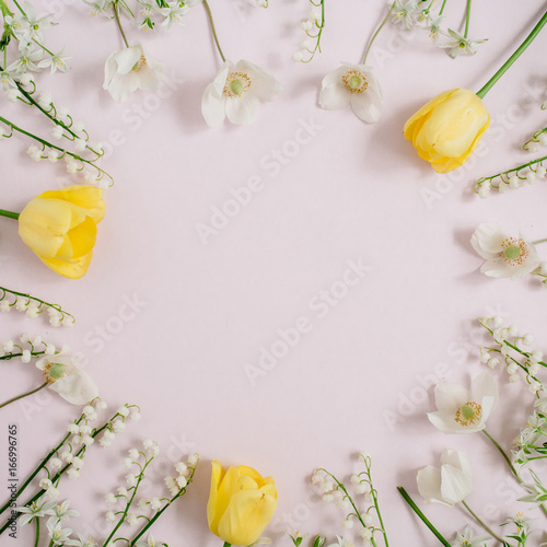 Fototapeta Naklejka Na Ścianę i Meble -  Frame of lily of the valley, yellow tulips, green leaves with space for text on pink background. Flat lay, top view