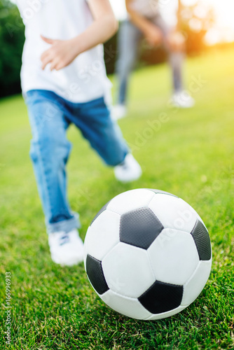 cropped shot of little boy playing soccer with ball on green lawn