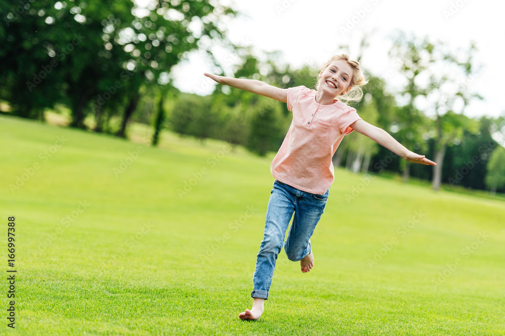 adorable happy little girl with open arms running on green grass in park