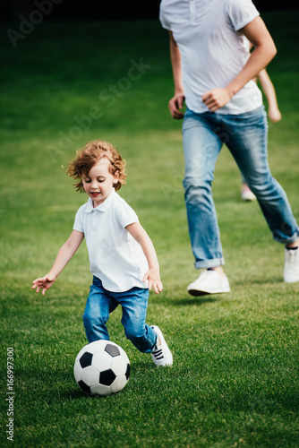 cropped shot of cute little boy with father playing soccer in park