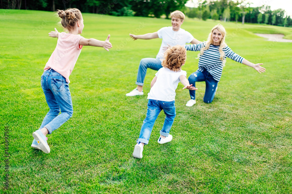 Fototapeta premium happy parents with open arms looking at cute little children running on grass