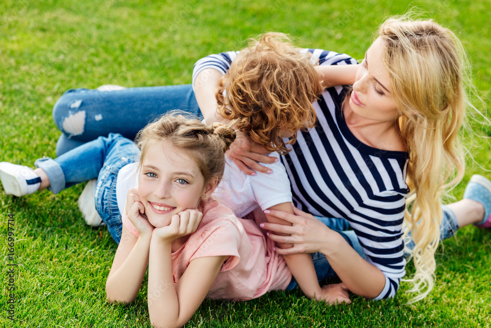 Fototapeta premium young mother with cute little children lying on green grass while resting in park