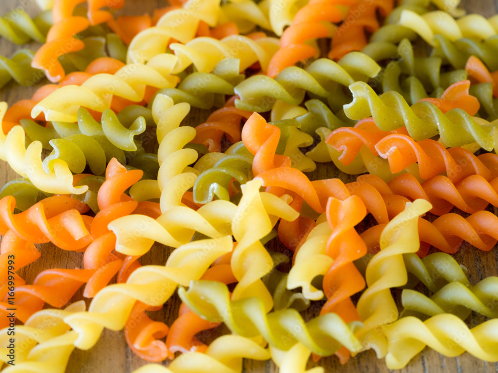 Background of colorful pasta texture close-up. close up of a dried italian pasta on a wooden table.Colored natural pasta Background of colorful pasta texture close-up. close up of a dried italian pasta on a wooden table.Colored natural pasta