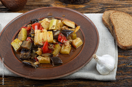 Vegetable stew with tomato, eggplant, zucchini, onion, carrot, pepper, close-up on a clay plate.