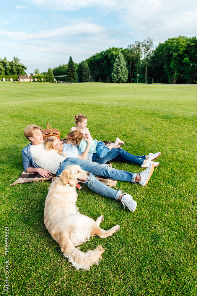 Obraz premium happy young family with golden retriever dog resting on grass at picnic