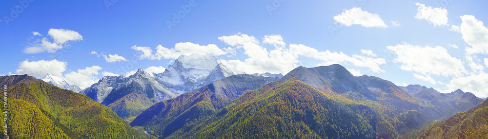 Shangri la, a panorama view of holy snow-clad mountain Chanadorje and yellow orange colored autumn trees in the valley in Yading national level reserve, Daocheng, Sichuan Province, China.