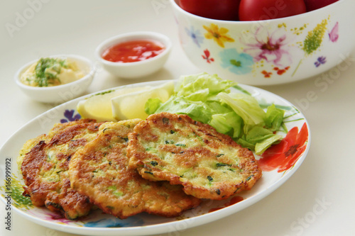 Zucchini pancakes. Vegetable fritters served with lemon and fresh salad. Yogurt and tomato sauces on background. Close up view. 
