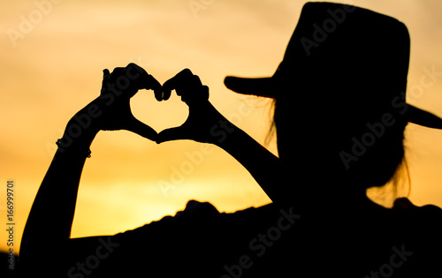 Girl making hearth shape, silhouette against golden sky
