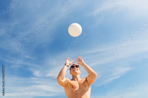 young man with ball playing volleyball on beach
